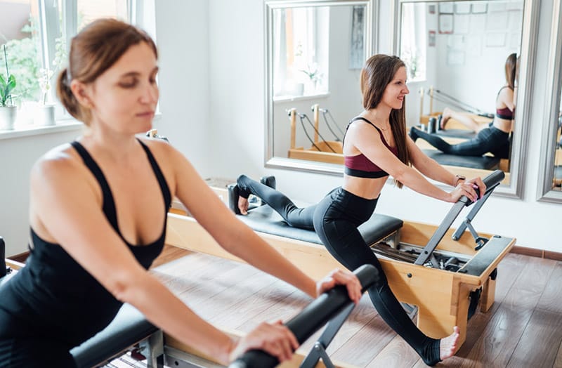 Two women taking a semi-private Pilates lesson on the reformer at Modus Pilates studio located in the Mile-Ex neighborhood of Montreal